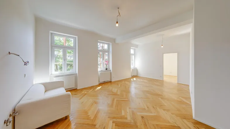 Helles Wohnzimmer mit Fischgrätparkett, hohen Decken und großen Fenstern.