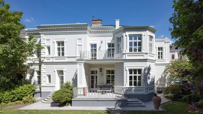 Elegante Villa mit klassischer Architektur, umgeben von einem gepflegten Garten und sonniger Terrasse.