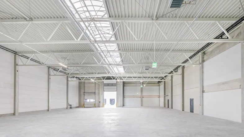 Weitläufige Industriehalle mit hohen Decken, Oberlichtern und großem Rolltor für den Zugang und die Logistik.