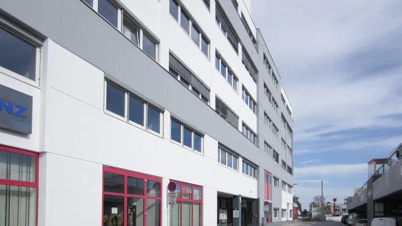 Modernes Geschäftsgebäude mit weißer und grauer Fassade sowie roten Akzenten an den Fenstern.