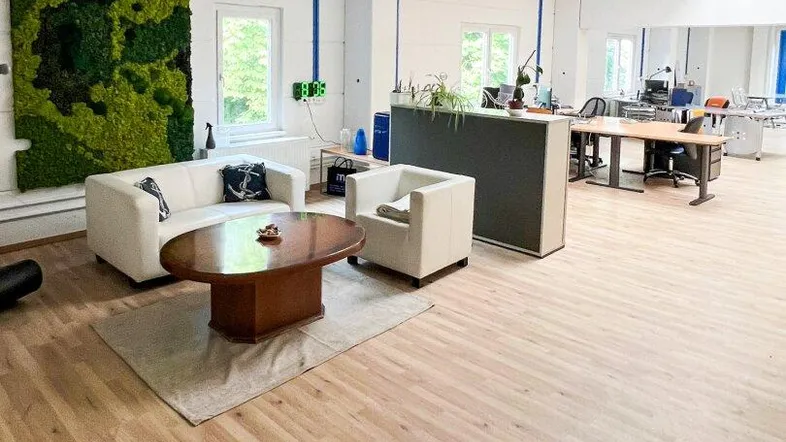 Geräumiger Bürobereich mit heller Holzoptikboden, bequemen Sitzgelegenheiten und dekorativer Mooswand.