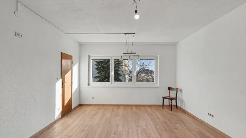 Geräumiger, leerer Raum mit Laminatboden und einem großen Fenster, das den Blick nach draußen freigibt.