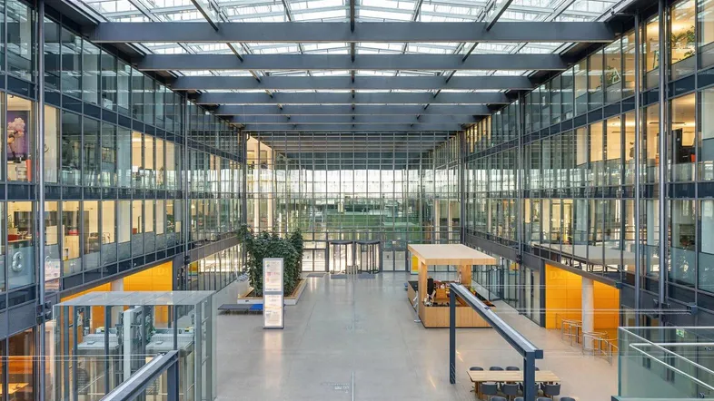 Großzügiges, modernes Atrium mit Glasdach, vielen Büroetagen und hellem Empfangsbereich.