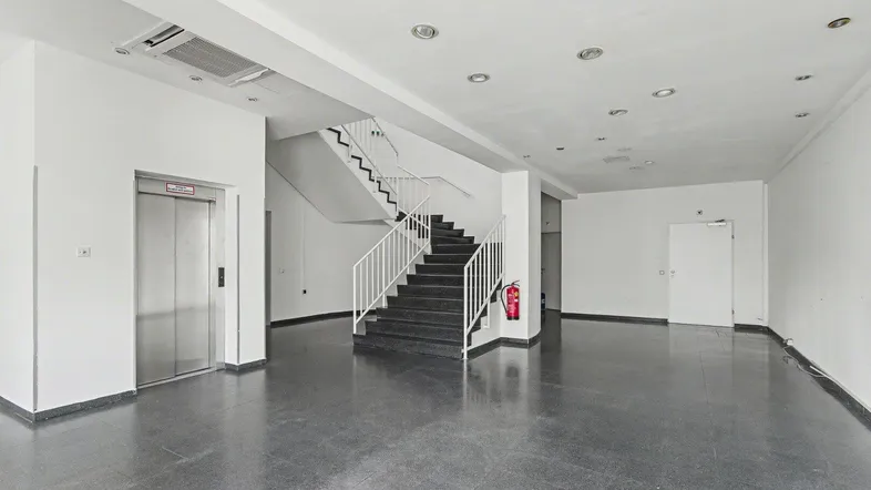 Geräumige Lobby mit Aufzug und Treppenhaus, ausgestattet mit dunklem Fliesenboden und heller Beleuchtung.