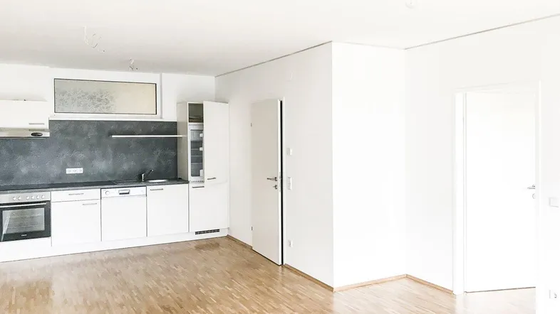 Heller offener Wohnbereich mit integrierter Küche, weißen Schränken und Parkettboden.