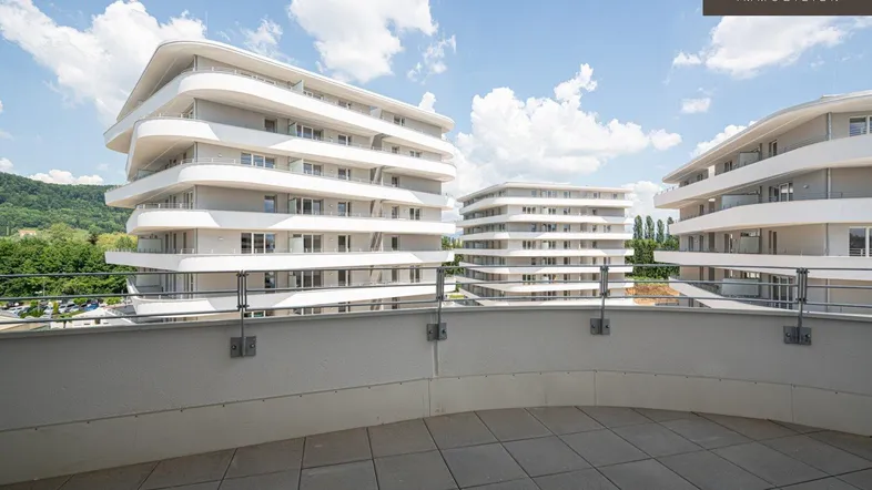 Große Terrasse mit Blick auf moderne Wohngebäude und den Himmel, ideal für Entspannung im Freien.