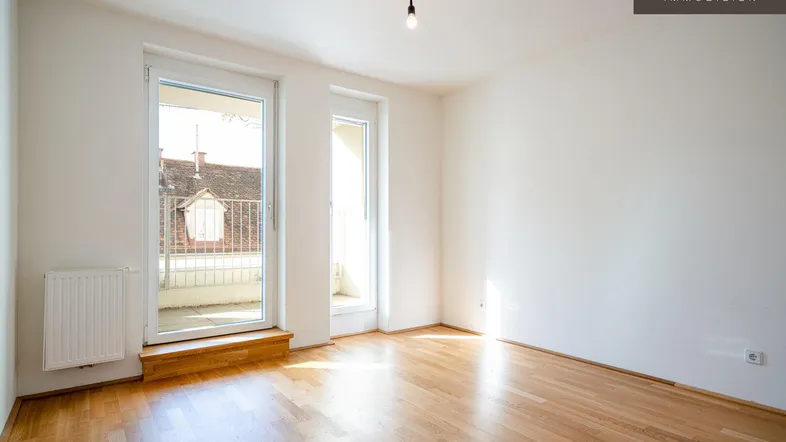 Helles Zimmer mit Parkettboden und Zugang zu einem kleinen Balkon, ideal als Wohn- oder Schlafzimmer.