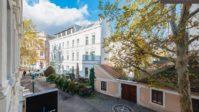 Blick auf eine charmante Kopfsteinpflasterstraße mit historischen Gebäuden und herbstlichen Bäumen.