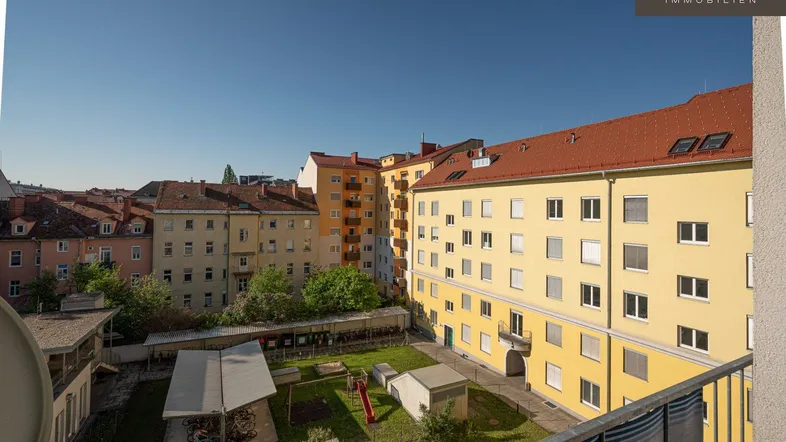 Blick von einem Balkon auf einen grünen Innenhof mit Spielplatz und umliegenden Wohngebäuden.