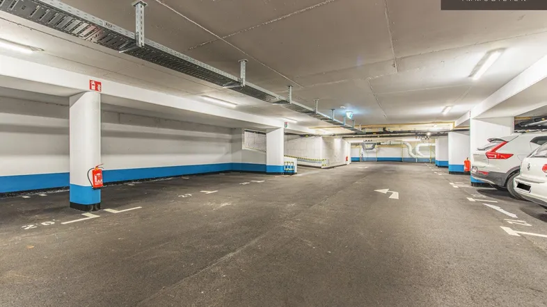 Geräumige Tiefgarage mit vielen Stellplätzen, klarer Markierung und sichtbaren Installationen an der Decke.