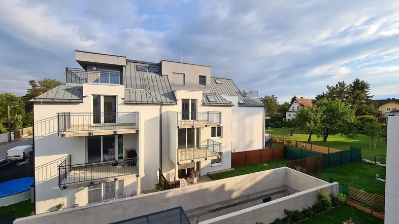 Modernes Mehrfamilienhaus mit mehreren Balkonen und einer kleinen Grünfläche im Vordergrund.