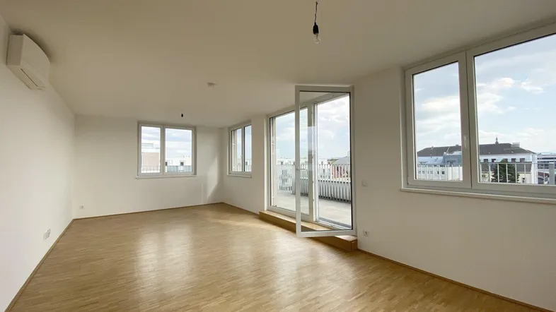 Helles, leeres Wohnzimmer mit Parkettboden, großen Fenstern und Zugang zur Terrasse.
