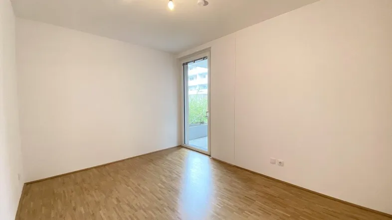 Helles, unmöbliertes Zimmer mit Parkettboden und direktem Zugang zu einem Außenbereich.