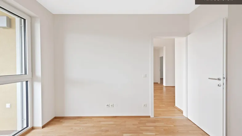 Heller, leerer Raum mit weiß gestrichenen Wänden, Holzfußboden und großem Fenster.