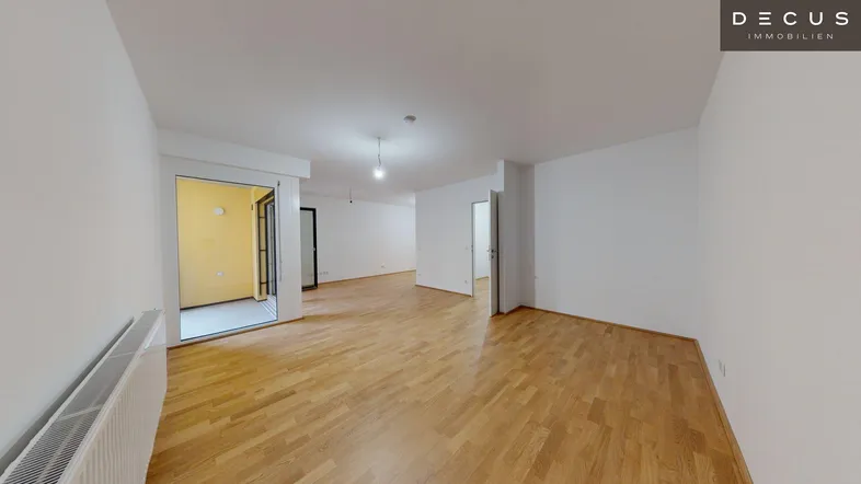 Heller Wohnbereich mit Parkettboden und Zugang zu einem Balkon, ideal für offenes Wohnen.
