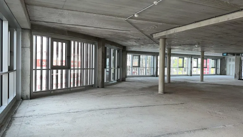 Großer, unfertiger Büroraum mit Sichtbetonflächen, hohen Decken und vielen Fenstern für natürliches Licht.