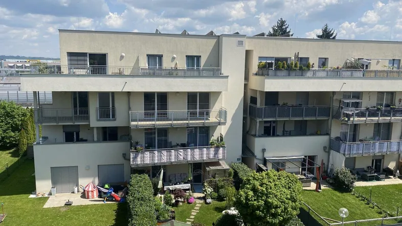 Moderne Wohnanlage mit mehreren Balkonen und privaten Gärten im Erdgeschoss unter bewölktem Himmel.