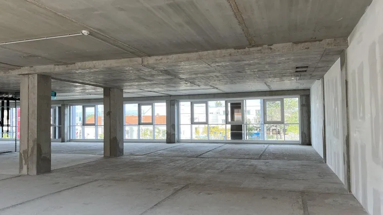 Großer, unfertiger Büroraum mit Betonboden, hohen Decken und vielen Fenstern, bereit für den Ausbau.