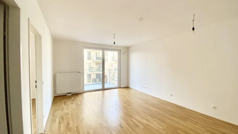 Helles, leeres Wohnzimmer mit Parkettboden und Zugang zu einem Balkon, bereit zur Einrichtung.