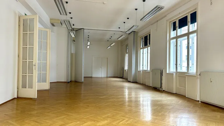 Großer, leerer Raum mit Fischgrätparkett und hohen Fenstern, ideal für Büronutzung.
