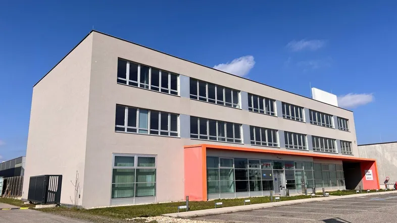 Modernes Bürogebäude mit heller Fassade und großen Fenstern unter blauem Himmel.