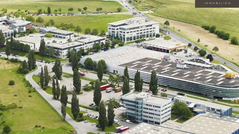 Luftaufnahme eines Gewerbegebiets mit mehreren Bürogebäuden, Parkplätzen und grünen Flächen.