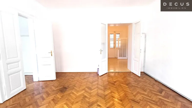 Helles Zimmer mit Fischgrätparkettboden und mehreren geöffneten Türen zu angrenzenden Räumen.