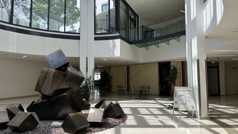 Großzügiges Atrium mit moderner Skulptur, viel Tageslicht und Zugang zu verschiedenen Bereichen.