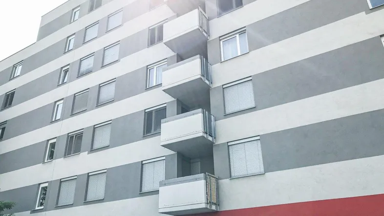 Mehrstöckiges Wohngebäude mit Balkonen und gestreifter Fassade unter hellem Himmel.