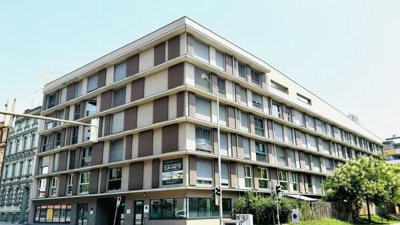 Modernes Eckgebäude mit mehreren Etagen und großen Fenstern in städtischer Umgebung.