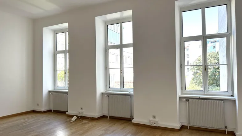 Heller Büroraum mit Holzboden und großen Fenstern, die viel Tageslicht hereinlassen.