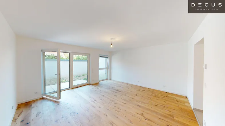 Helles, leeres Zimmer mit Holzboden und Zugang zum Außenbereich durch große Glastüren.