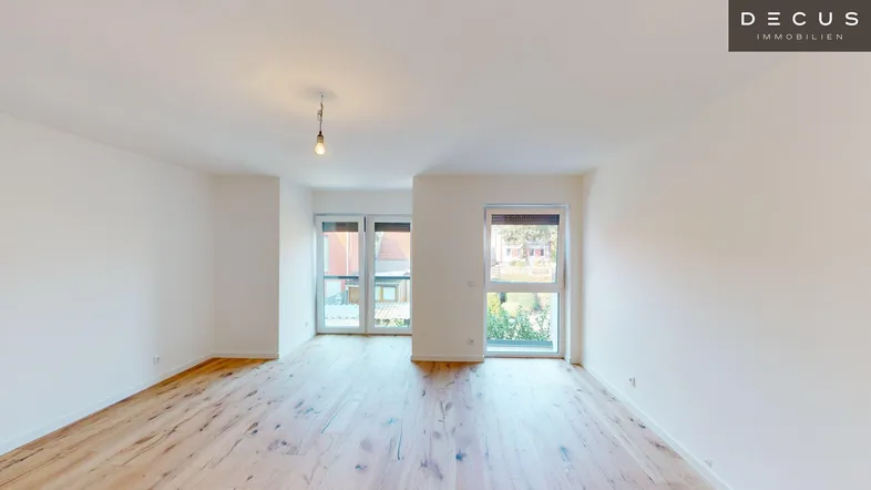 Heller, leerer Wohnbereich mit Holzboden und großen Fenstern, die viel Tageslicht hereinlassen.