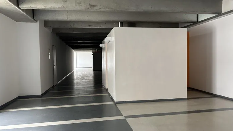 Langer Flur in einem Bürogebäude mit sichtbaren Betondecken und funktionaler Beleuchtung.