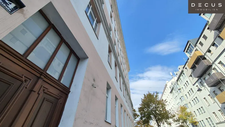 Blick auf die historische Fassade eines Mehrfamilienhauses mit Holztür und Fenstern unter blauem Himmel.