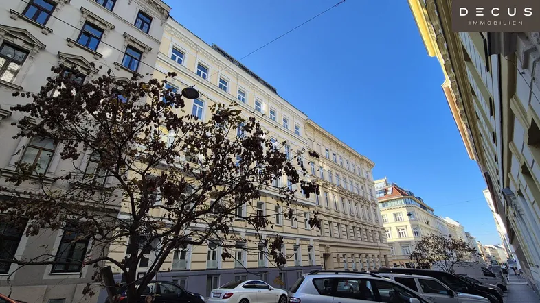 Blick auf die historische Fassade eines Mehrfamilienhauses mit parkenden Autos auf der Straße.