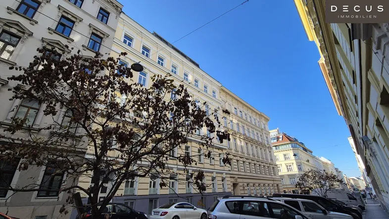 Historisches Gebäude mit klassischer Fassade und parkenden Autos an einer städtischen Straße.