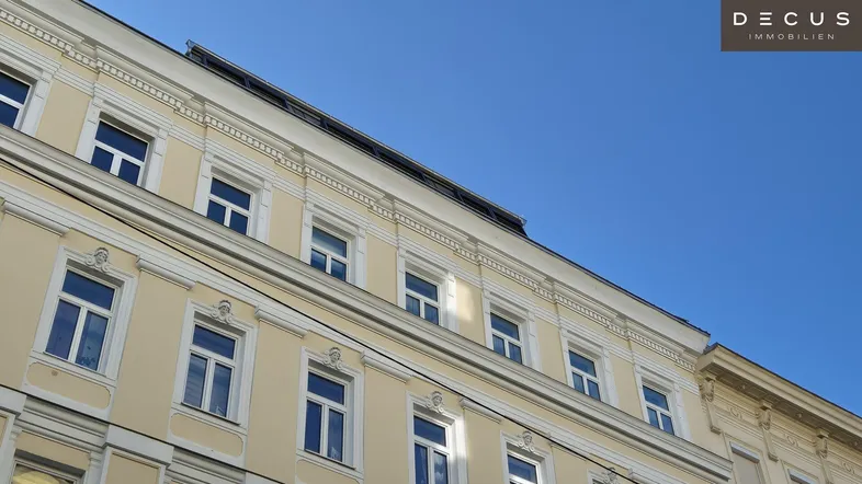 Gelbe Fassade eines Mehrfamilienhauses mit vielen Fenstern unter blauem Himmel.
