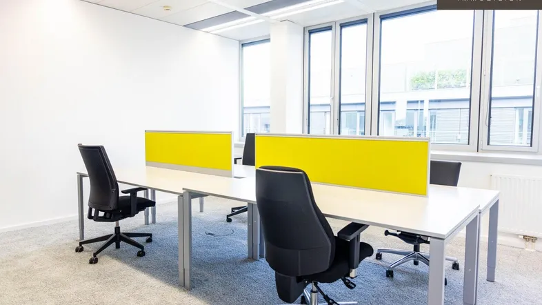 Heller Großraumbüro-Arbeitsbereich mit modernen Schreibtischen, ergonomischen Stühlen und großen Fenstern für viel Tageslicht.