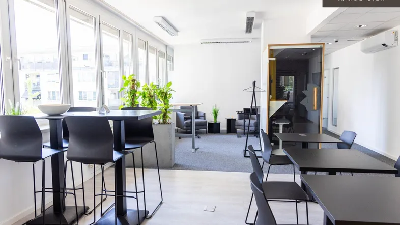 Moderner Büroraum mit hohen Tischen, Barhockern und einem Lounge-Bereich, der viel Tageslicht erhält.