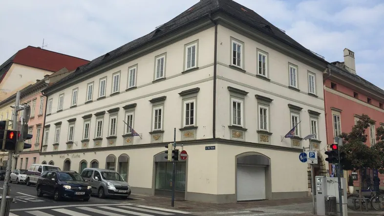 Historisches Eckgebäude an einer belebten Straße mit klassischer Architektur und vielen Fenstern.