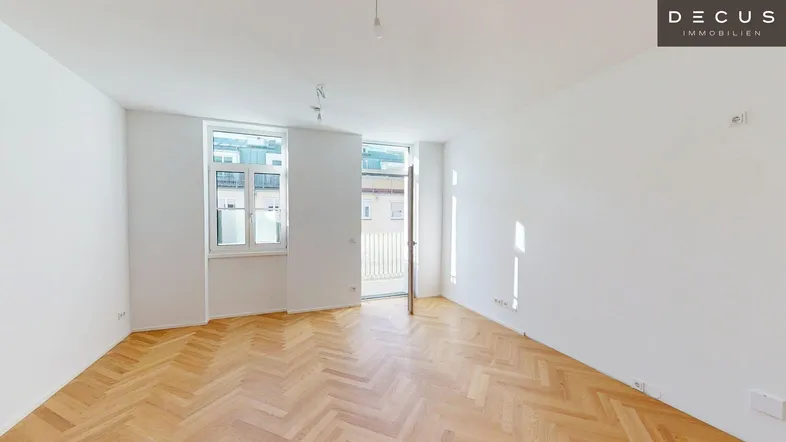 Heller Wohnraum mit Fischgrätparkettboden und Zugang zu einem Balkon oder einer Terrasse.
