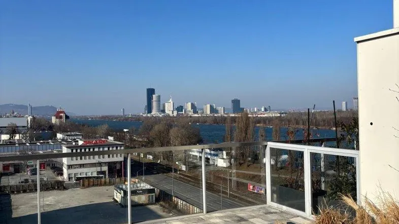 Große gepflasterte Terrasse mit Glasgeländer und weitem Blick auf die Stadt und den Fluss.