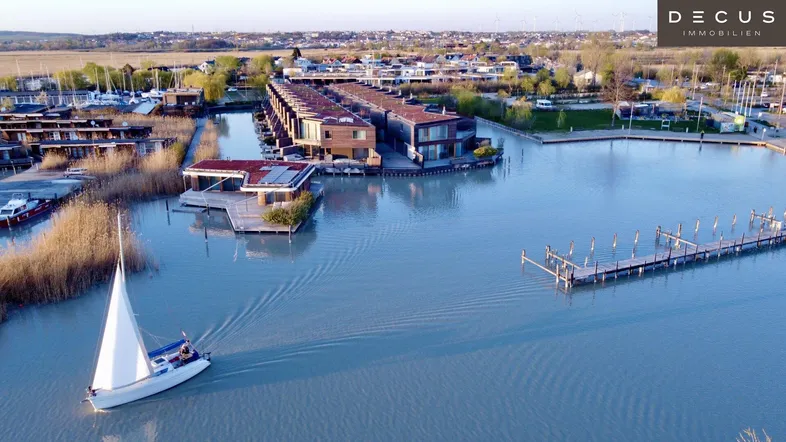 Luftaufnahme der modernen schwimmenden Häuser am See mit einem Segelboot und Stegen.