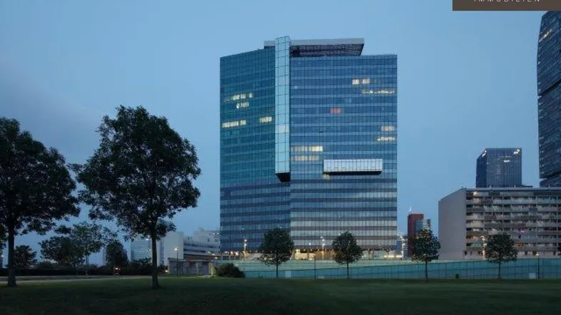 Modernes Hochhaus mit Glasfassade und umliegender Grünfläche bei Dämmerung in städtischer Umgebung.