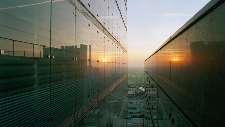 Moderne Glasfassade eines Bürogebäudes bei Sonnenuntergang mit Blick auf die Stadt.