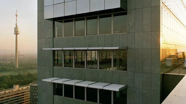 Modernes Hochhaus mit Glasfassade und Blick auf die Stadt bei Sonnenuntergang.
