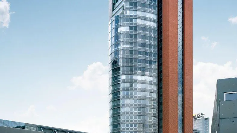 Moderne Hochhäuser mit Glasfassade und Backsteinturm in einer städtischen Umgebung unter blauem Himmel.