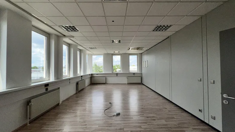 Geräumiges Büro mit Laminatboden, großen Fenstern und abgehängter Decke, ideal für flexible Arbeitsplatzgestaltung.