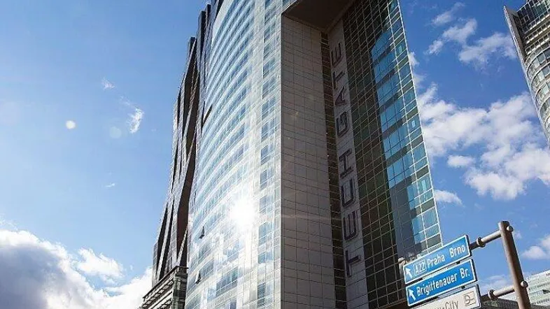 Modernes Hochhaus mit Glasfassade und geschwungener Architektur, umgeben von einer städtischen Straße unter blauem Himmel.